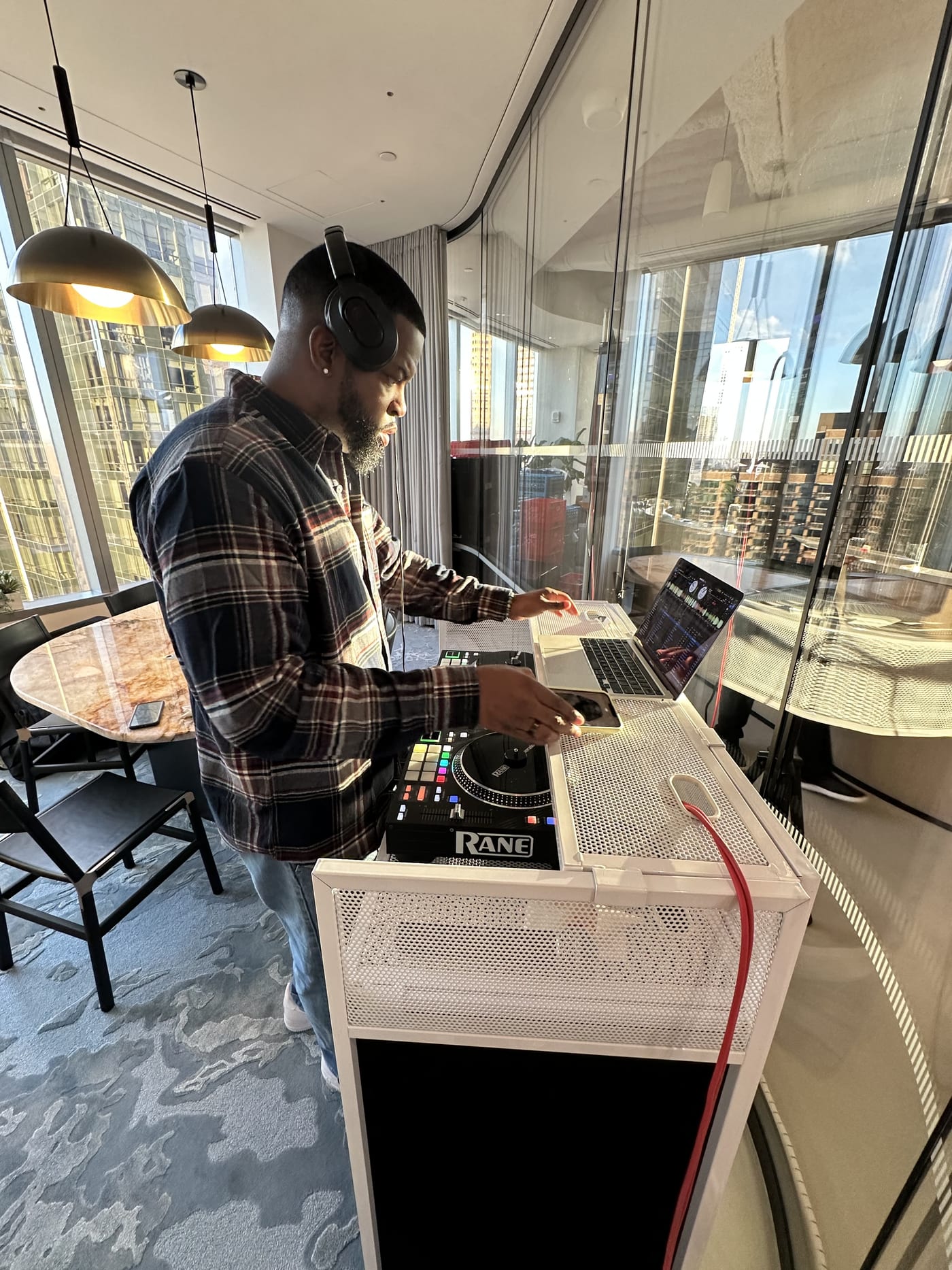 Holiday party DJ — DJ DX behind the decks at a corporate office party in Midtown Manhattan with skyline windows behind the booth