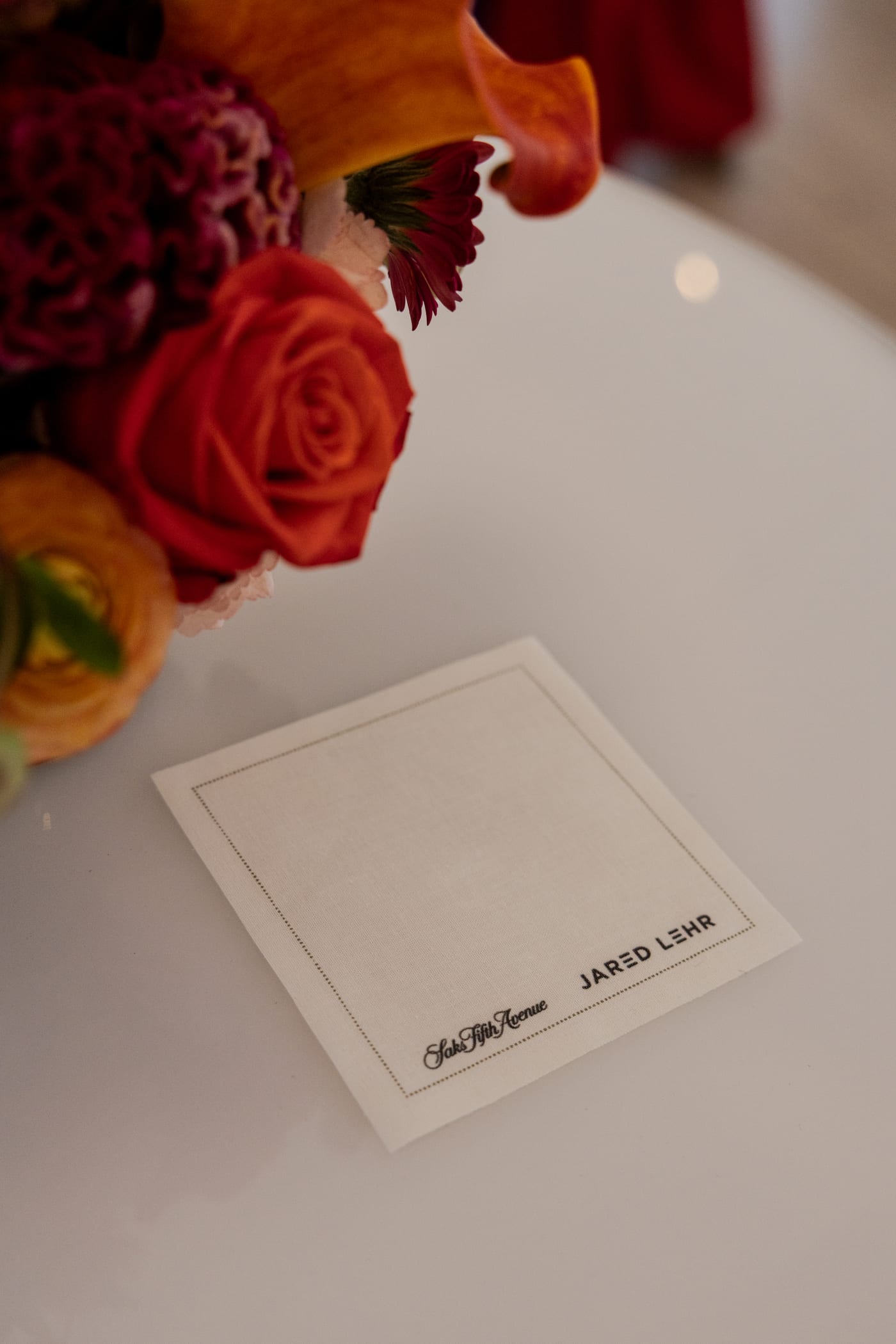 Saks Fifth Avenue and Jared Lehr co-branded place card beside florals at a private estate event in Water Mill, New York