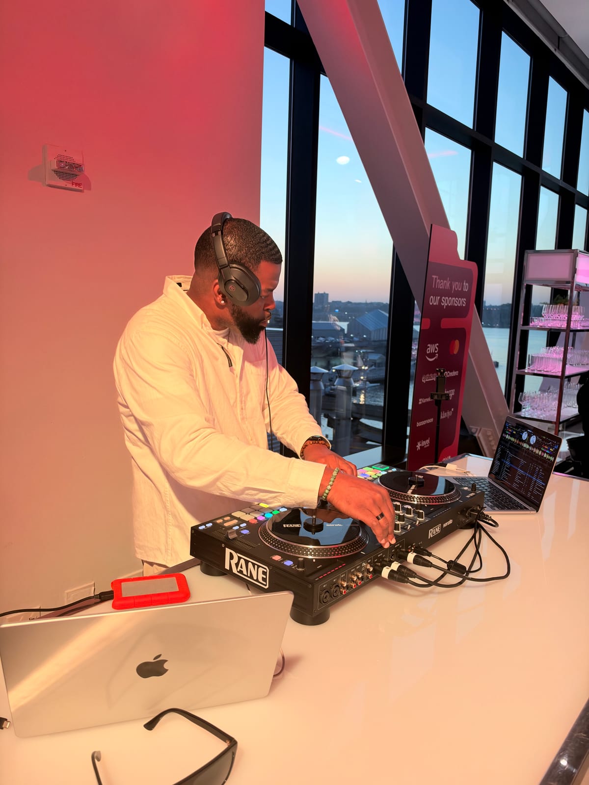 DJ DX at the decks at Contentsquare's CX Circle NYC 2026, The Glasshouse, Hell's Kitchen, with the Hudson River at sunset behind him